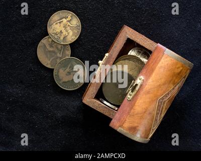 Vari vecchi penny sudafricani ben utilizzati in un piccolo scrigno di legno su sfondo nero Foto Stock