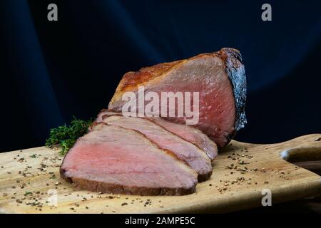 Primo piano di una giuntura di succosa roast beef irlandese affettato su un piatto di legno. Foto Stock