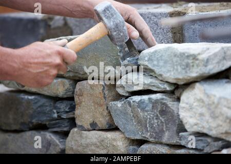 Close-up shot di uno scalpellino la costruzione di un muro di pietra. Foto Stock
