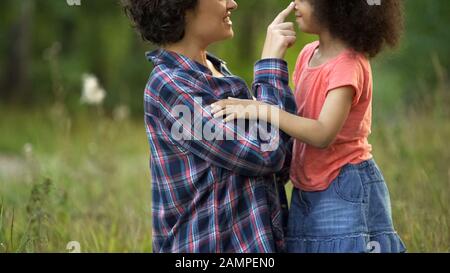Madre giovane e figlia piccola cute nuzzando e ridendo insieme, felicità Foto Stock