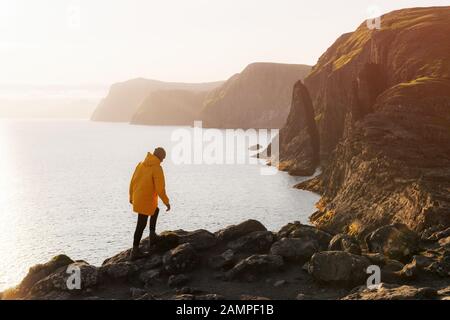 Tourist in giacca gialla guarda le scogliere vicino al lago di Sorvagsvatn sull'isola di Vagar, le Isole Faroe, Danimarca. Fotografia di paesaggio Foto Stock