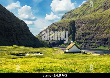Vista estiva della tradizionale chiesa turf-top Saksunar Kirkja nel villaggio di Saksun. Paesaggio di bellezza con Pollurin Laguna e alte montagne. Isola Streymoy, Isole Faroe, Danimarca. Foto Stock