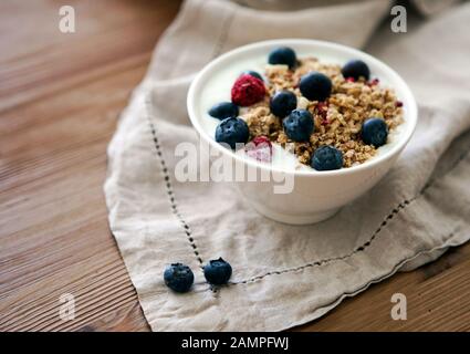 Deliziosa ciotola per la colazione allo yogurt con muesli e more fresche su un tavolo in legno e biancheria da cucina-asciugamano. Concetto di nutrizione sana e organica Foto Stock