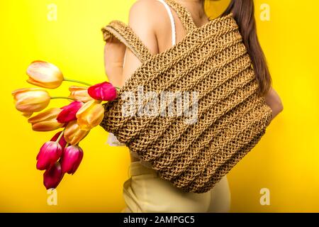 Vendita primaverile nei negozi. Accessori per sacchetti di paglia. Donna che tiene borsa di paglia con tulipani. Moda giorno donne Foto Stock