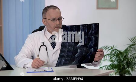 Chirurgo spinale che esamina la risonanza magnetica dorsale, prendendo appunti nella cartella clinica dei pazienti Foto Stock