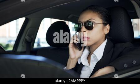 Lady in occhiali da sole seduti in auto e parlare al cellulare, agente di polizia in servizio Foto Stock