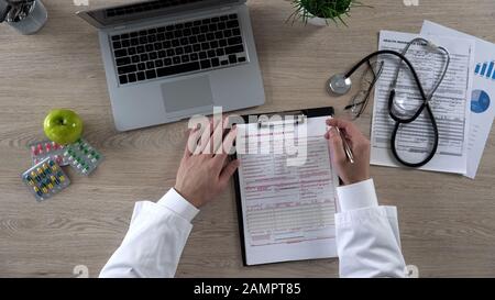 Il medico generico che legge il modulo di reclamo di assicurazione contro le malattie prima della firma della vista superiore Foto Stock