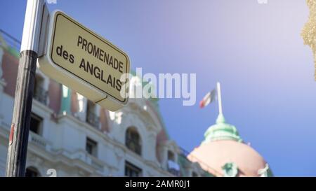 Segnale Promenade des Anglais Street, bandiera francese che sventola in cima all'edificio di Nizza Foto Stock