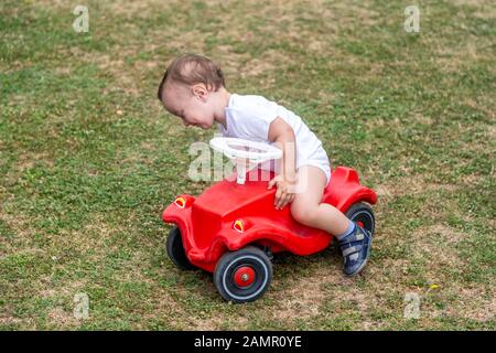 Ragazzino seduto su un'auto giocattolo in plastica che gioca fuori. Foto Stock