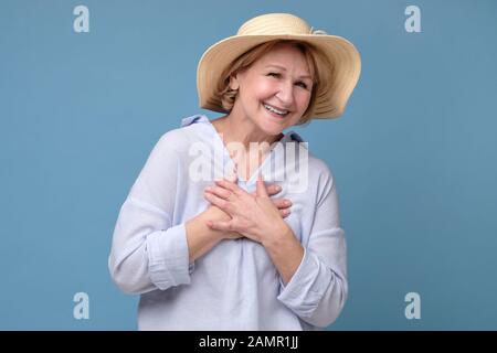 Felice gioiosa signora senior in estate cappello guardando la macchina fotografica e sorridente isolato su sfondo blu Foto Stock