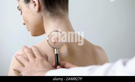 Terapista che esamina la ferita sulla spalla femminile con lente d'ingrandimento, assistenza sanitaria Foto Stock