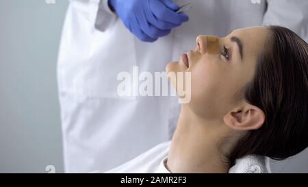 Signora con intonaco sul naso, medico che esamina il viso dei pazienti dopo chirurgia plastica Foto Stock