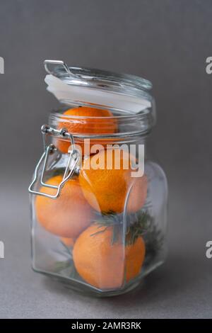 Tangerini organici freschi con rami di abete rosso in un vaso (banca) con una staffa di blocco su sfondo grigio. L'idea di confezionare un regalo nello stile. Foto Stock