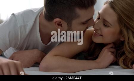 Giocoso giovane coppia sdraiata a letto, nuzzling, felice amorevole relazioni, luna di miele Foto Stock