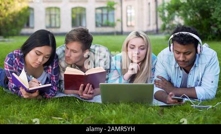 Gruppo di amici sdraiati sul prato del campus e preparati per la prova, la vita degli studenti Foto Stock