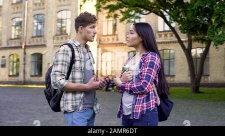 Studente maschio che parla con bella amica femminile, che discute di test vicino al college Foto Stock