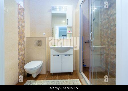 Sala da bagno nell'appartamento. Doccia, Lavandino Con Specchio, Wc. Quadrati di piastrelle in ceramica in forma di blu, giallo, rosso e bianco di modelli di foglia sulla parete Foto Stock