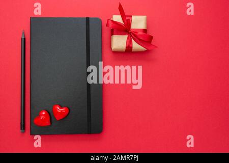 Notebook nero su sfondo rosso con due cuori e confezione regalo. Concetto di San Valentino. Foto Stock