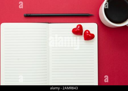 San Valentino. Apri il notebook con i cuori rossi e una matita, sullo sfondo rosso, copia spazio per il testo. Foto Stock