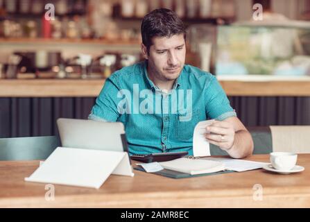 Imprenditore che gestisce la sua piccola impresa - Uomo D'Affari che guarda sopraffatto - giovane proprietario della caffetteria che passa attraverso la documentazione Foto Stock