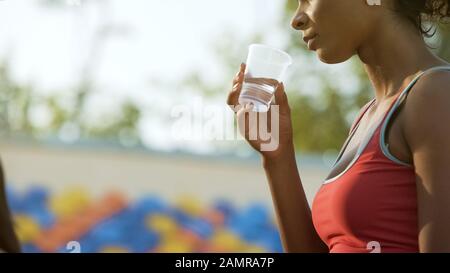 Ragazza biraciale bere dopo l'allenamento, ripristinare l'equilibrio dell'acqua, idratazione Foto Stock