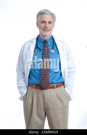 Scatto verticale di un medico maturo allegro che si alza con le mani in tasca. Indossa un camice da laboratorio bianco e ha uno stetoscopio intorno al collo Foto Stock