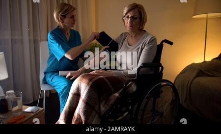 Donna infermiera che misura la pressione sanguigna della donna, l'ipertensione, la mancanza di speranza della vecchiaia Foto Stock