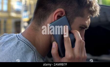 Male uomo che parla sullo smartphone, in piedi vicino alla sua auto rotta, rottura Foto Stock