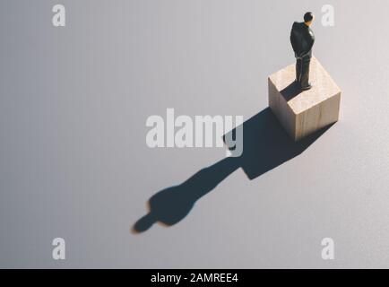 uomo d'affari in miniatura su cubo di legno contro la luce dura con ombra lunga Foto Stock