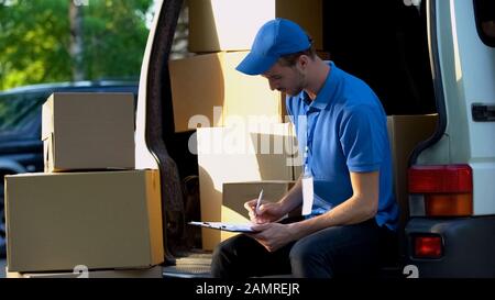 Lavoratore di ufficio postale contando scatole di cartone riempire rapporto di inventario, servizio Foto Stock