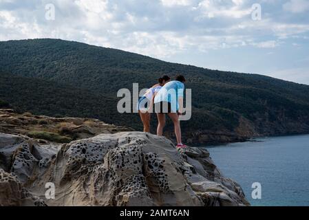 Uomo e donna in piedi su rocce che si affacciano sul mare, Golfo di Baratti, Italia Foto Stock