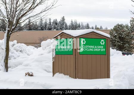 Un cestino di cestino per vestiti e scarpe si trova in un parcheggio coperto di neve in una città di montagna americana nord-occidentale durante l'inverno. Foto Stock