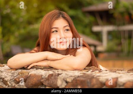 Donna asiatica in piedi, sorridente e guardando nell'occhio. Foto Stock