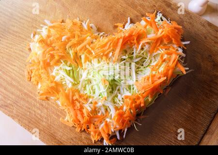 Cavolo bianco e carote finemente tritate a forma di cuore. Concetto di amore per la cucina vegetariana e verdure crude. Foto Stock