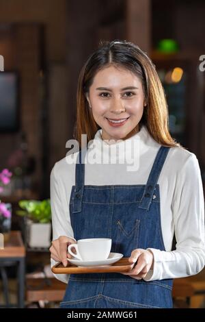 Ritratto di un bel barista asiatico che tiene una tazza di caffè nel caffè Foto Stock