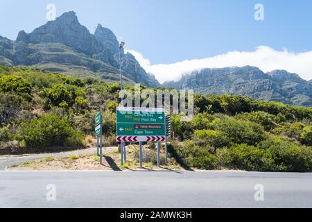 Cartello verde sulla M62 strada principale,Camps Bay Drive,che mostra le direzioni di Hout Bay e Cape Town con Table Mountain e funivia stazione superiore dietro Foto Stock