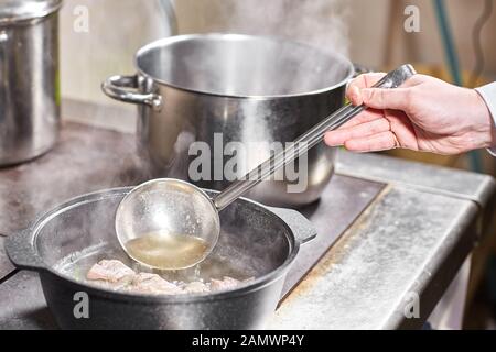 chef cuoco aggiunge gli ingredienti. brodo di manzo tradizionale con verdure, ossa e ingredienti in pentola, ricetta di cottura. Zuppa in una pentola di cottura con mestolo Foto Stock