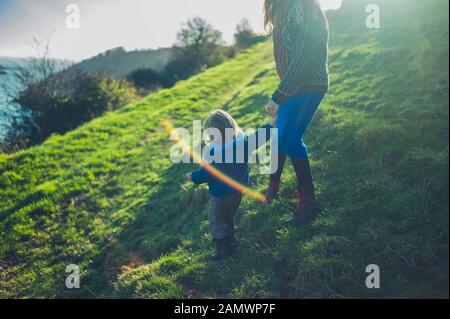 Una giovane madre e il suo bambino camminano su una collina al tramonto in inverno Foto Stock