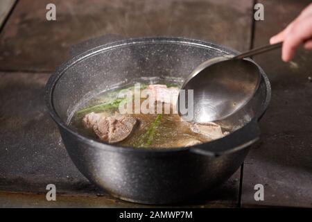 chef cuoco aggiunge gli ingredienti. brodo di manzo tradizionale con verdure, ossa e ingredienti in pentola, ricetta di cottura. Zuppa in una pentola di cottura con mestolo Foto Stock