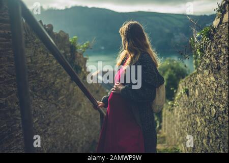 Una giovane donna incinta sta camminando su alcune scale all'aperto in un piccolo villaggio in una giornata invernale Foto Stock