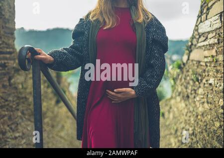 Una giovane donna incinta sta camminando su alcune scale all'aperto in un piccolo villaggio in una giornata invernale Foto Stock