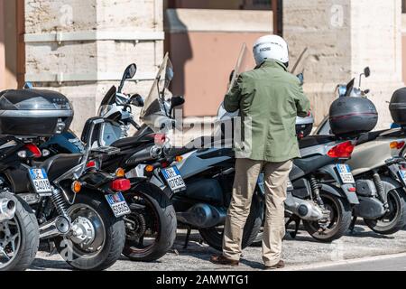 Perugia, Italia - 29 agosto 2018: Molti ciclomotori per motociclette parcheggiati nel parcheggio di strada della città con l'uomo in piedi nel casco durante il giorno estivo Foto Stock