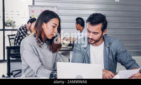 Creative designer riunione informale con il computer portatile alla scrivania in ufficio moderno.collega la discussione circa il progetto di lavoro.informale stile di vita sul posto di lavoro. Foto Stock