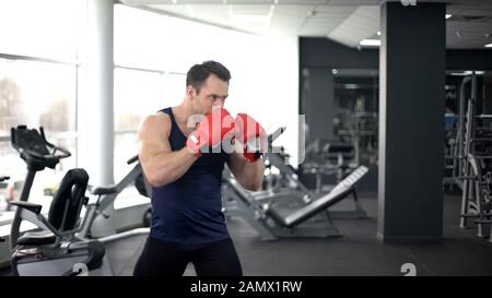 Pugile muscolare in guanti di allenamento in palestra, fare lotta, spirito sportivo Foto Stock