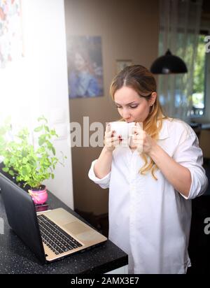 donna sorridente che lavora a casa e beve caffè Foto Stock