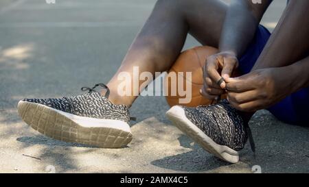 Giocatore di pallacanestro che lega le scarpe, primo piano delle gambe dell'uomo afro-americano Foto Stock