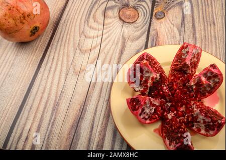 Mature succosa melagrana tagliata in più pezzi su una piastra di ceramica su uno sfondo di legno. Close up Foto Stock