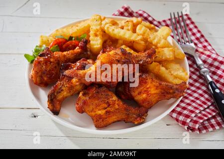 Spicy impanati ali di pollo con patatine fritte o incresparsi tagliata cotta al forno patatine fritte condite con erbe e spezie su una piastra con posate e tovagliolo Foto Stock