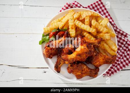 Alla brace croccanti ALI DI POLLO PICCANTI con cotta nel forno crinkle cut potato chips e insalata trimming su una piastra visto dal tettuccio Foto Stock