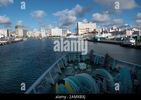 Vista urbano di Naha sull'isola di Okinawa, in Giappone, Asia. Città giapponese visto dalla nave che entra in porto. Mare e traghetto Foto Stock